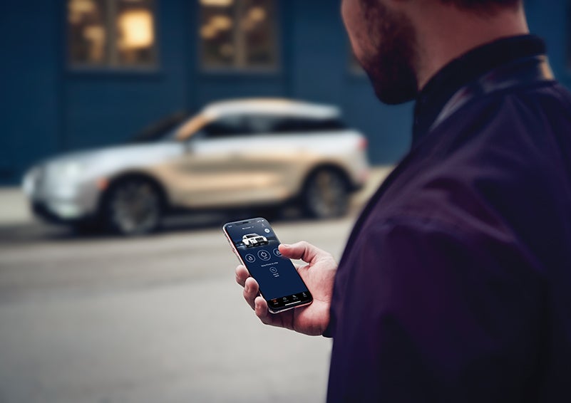 A person is shown interacting with a smartphone to connect to a Lincoln vehicle across the street. | Spitzer Lincoln DuBois in Du Bois PA
