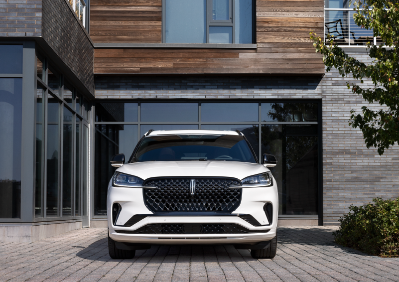 A white 2025 Lincoln Aviator® SUV is shown parked outside a modern building with gray brick and wood accents. | Spitzer Lincoln DuBois in Du Bois PA