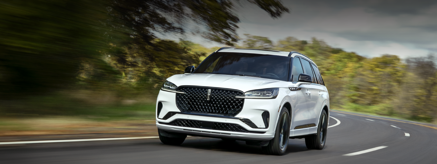 A white 2025 Lincoln Aviator® SUV is being driven down a road lined with trees. | Spitzer Lincoln DuBois in Du Bois PA