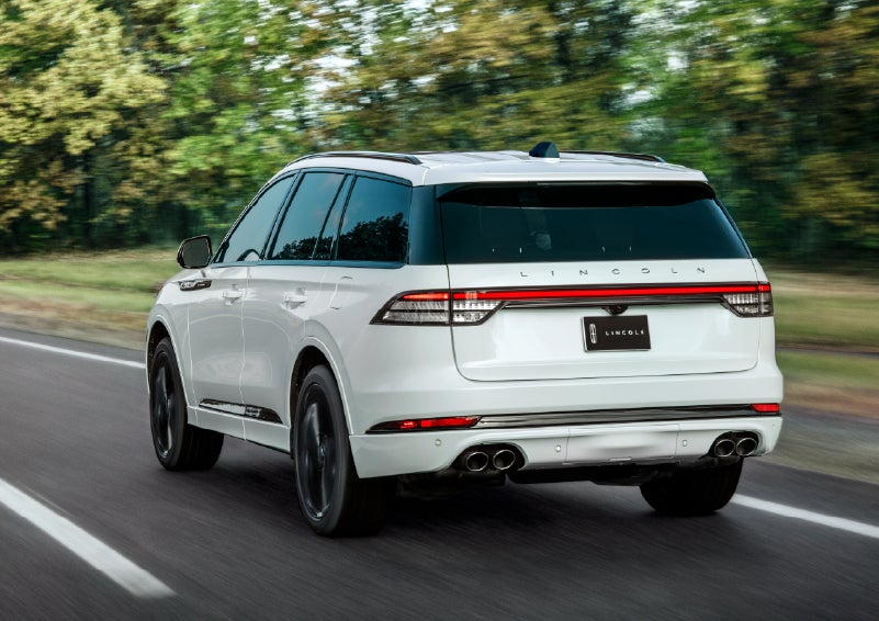 A white 2026 Lincoln Aviator® SUV is being driven away down a road lined with colorful trees. | Spitzer Lincoln DuBois in Du Bois PA