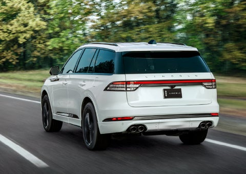 A white 2026 Lincoln Aviator® SUV is being driven away down a road lined with colorful trees. | Spitzer Lincoln DuBois in Du Bois PA
