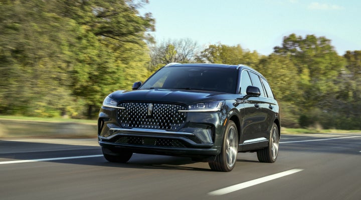 A 2026 Lincoln Black Label™ Aviator® SUV is being driven down a road lined with trees. | Spitzer Lincoln DuBois in Du Bois PA