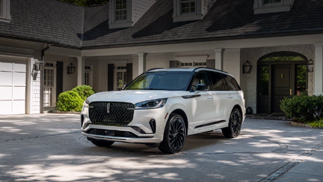 A white 2026 Lincoln Aviator® SUV is parked in the driveway of a luxury home. | Spitzer Lincoln DuBois in Du Bois PA