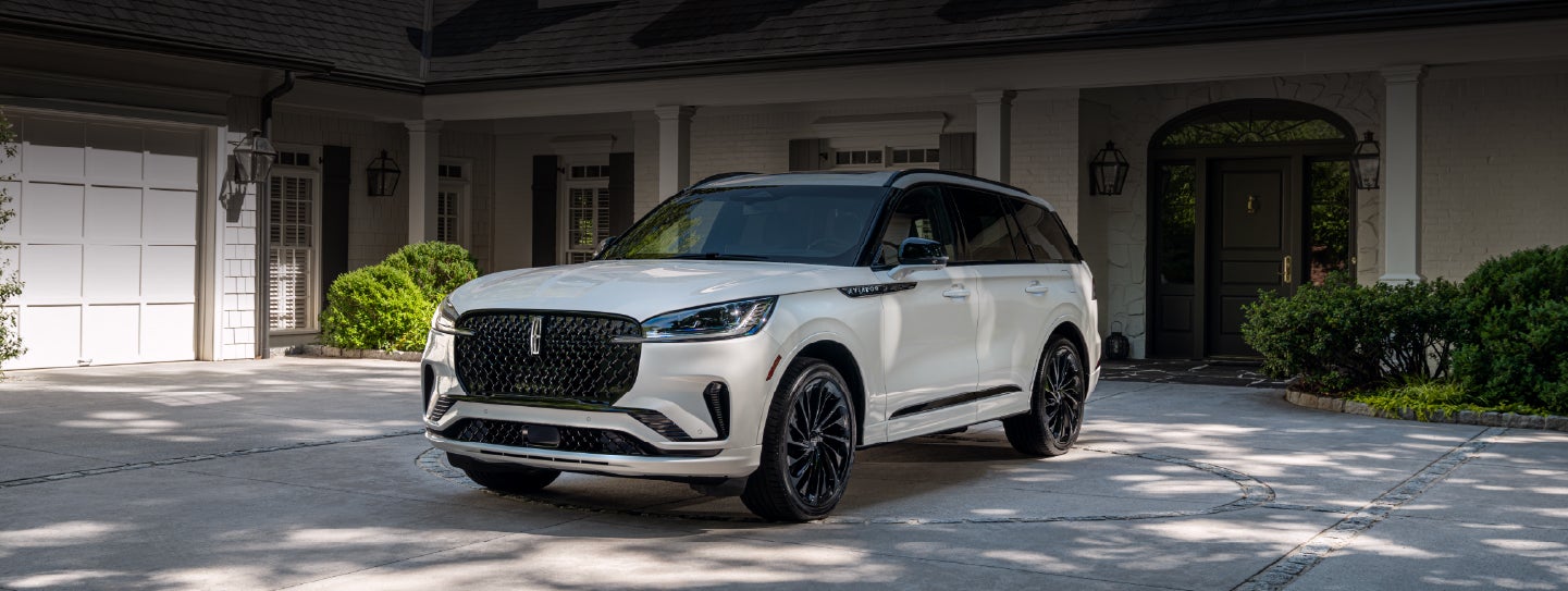 A white 2026 Lincoln Aviator® SUV is parked in the driveway of a luxury home. | Spitzer Lincoln DuBois in Du Bois PA